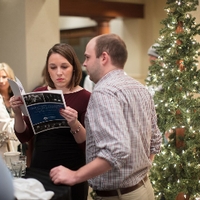 People standing near decorative christmas trees, looking through a program together